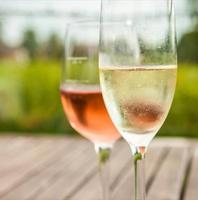 Two glasses of wine, one rose and one sparkling, on a wooden table over looking a field.